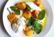A white bowl filled with peach, burrata, and basil salad.