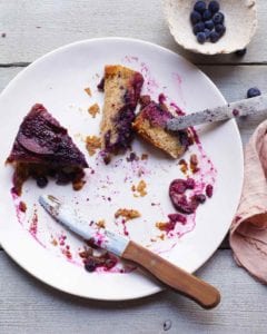 A couple slices of plum-blueberry upside-down cake on a white plate with a knife resting on the edge of the plate.