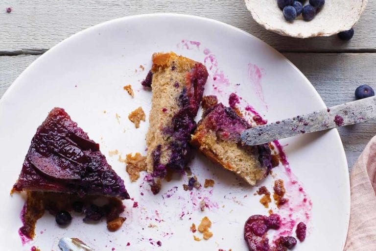 A couple slices of plum-blueberry upside-down cake on a white plate with a knife resting on the edge of the plate.