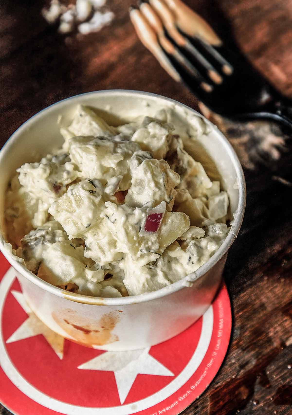 Potato Salad with Apples in a white serving bowl on top of a red and white star-patterned trivet.