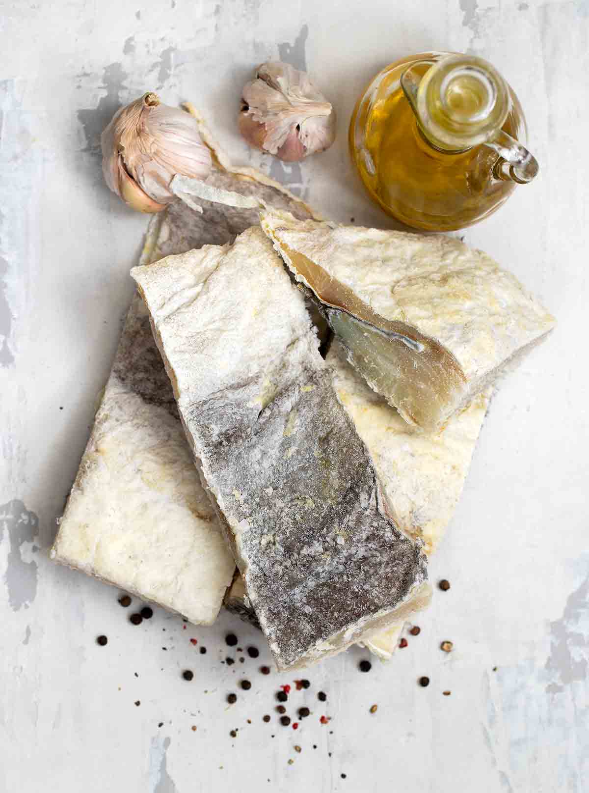 Salt cod fillets, garlic, and olive oil on marble.