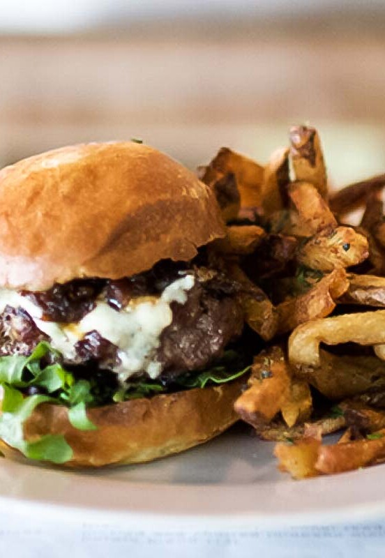 A skillet cheeseburger with arugula and a pile of fries on a white plate.