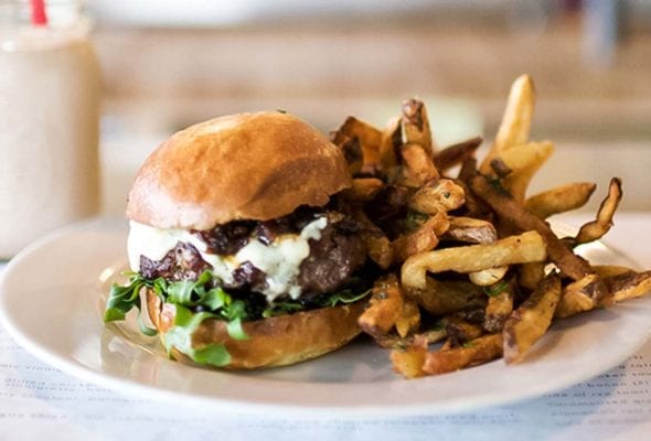 A skillet cheeseburger with arugula and a pile of fries on a white plate.