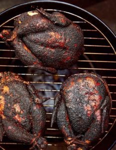 Three whole smoked chickens on a round grill.