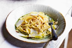 A bowl of spaghetti all'Aglio e Olio topped with olive oil and flakes of Parmesan cheese.