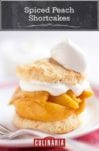 A spiced peach shortcake on a white plate with spiced peaches layered between two biscuit halves and topped with whipped cream.