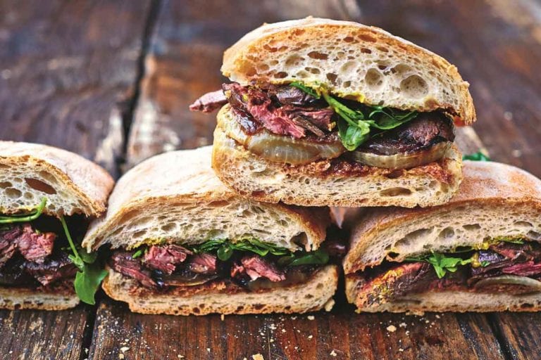 Steak sandwich pieces side-by-side and stacked on top of each other on a wooden table.