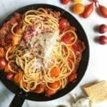 A black skillet filled with summer tomato pasta, sprinkled with fresh Parmesan cheese.