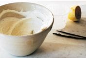 A bowl of sweet whipped ricotta cream, a halved lemon, two vanilla beans, a knife, and a small glass on a marble surface.