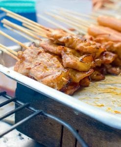 Skewers of thinly sliced Thai-style grilled pork skewers on a metal tray in a street food vendor's cart