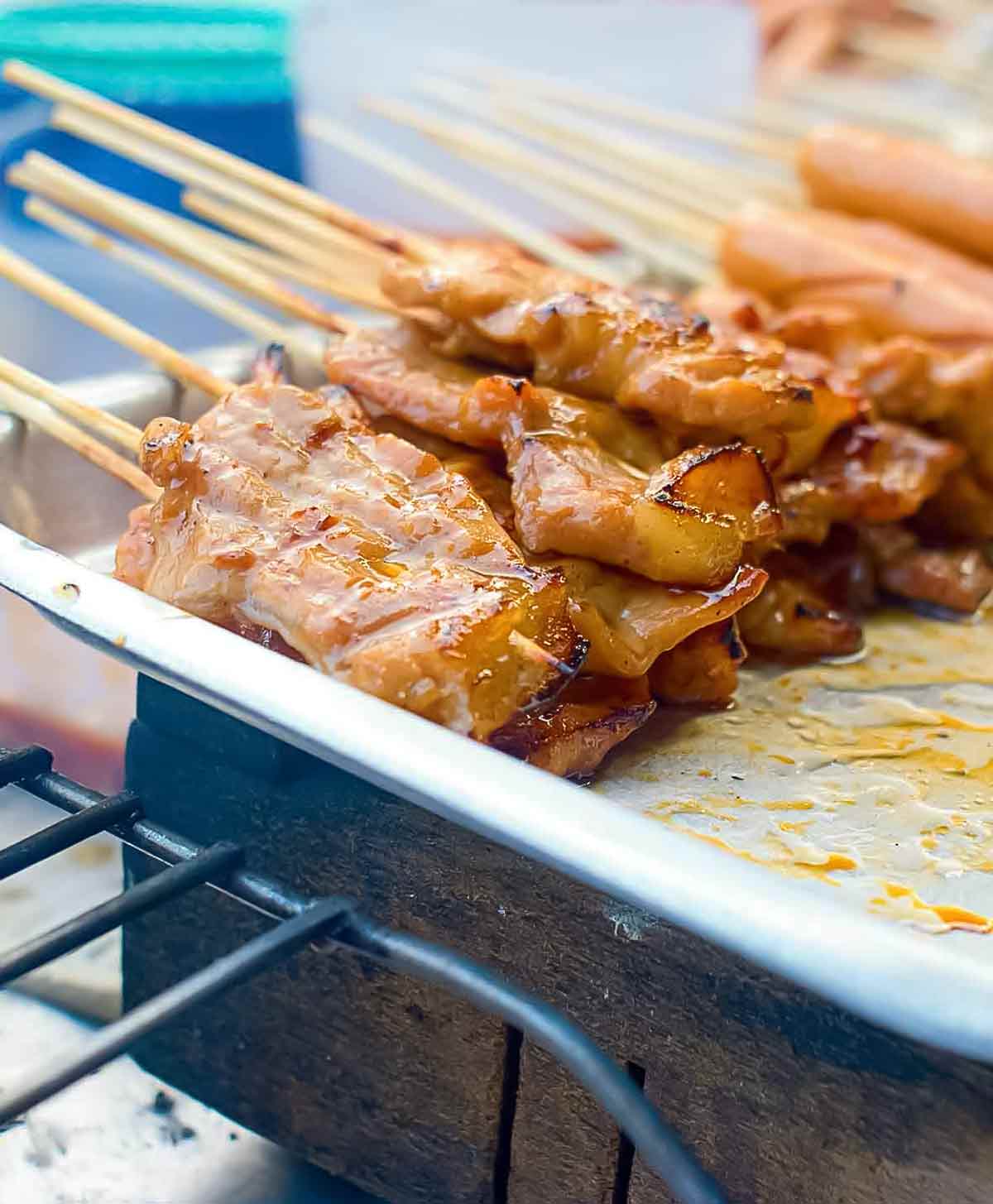 Skewers of thinly sliced Thai-style grilled pork skewers on a metal tray in a street food vendor's cart