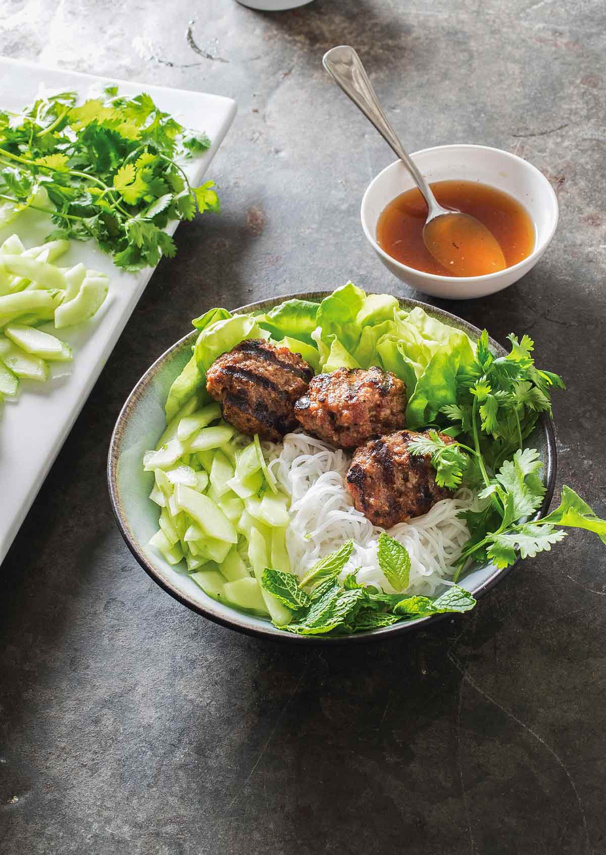 A dish filled with Vietnamese grilled pork patties with rice noodles and an crunchy vegetables.