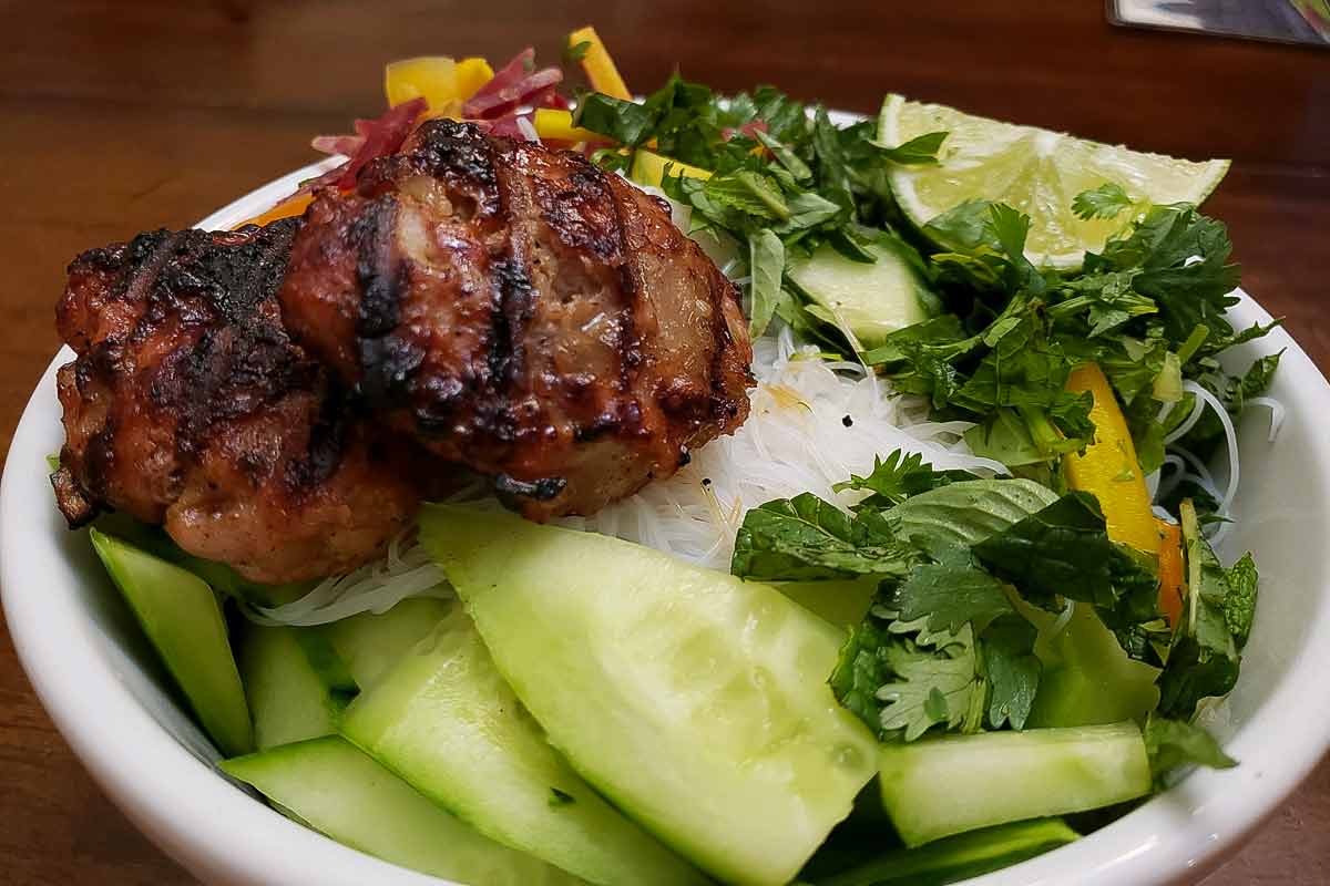 A dish filled with Vietnamese grilled pork patties with rice noodles and an crunchy vegetables.