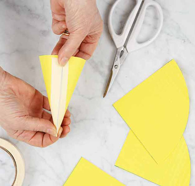 A person forming a waffle cone shaper with extra pieces of paper and scissors beside it.