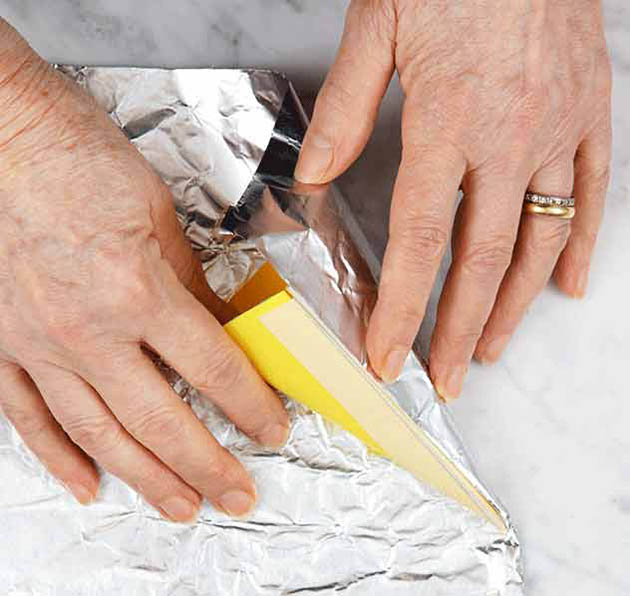 A person wrapping a waffle cone shaper in foil.