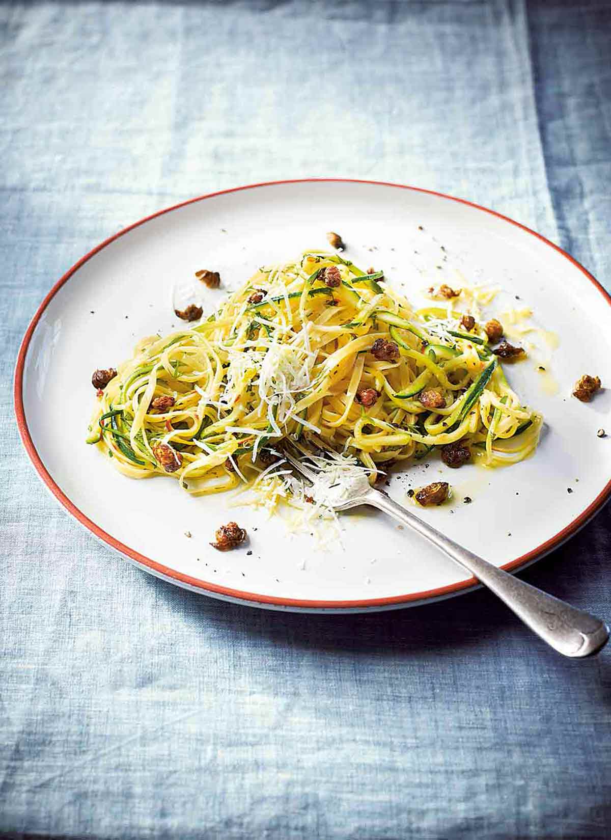 En vit tallrik zucchini-linguine--med pasta, zucchini, vitlök, kapris, mynta, dill och ost med en gaffel