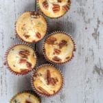 Five baked blueberry pecan muffins on a wooden surface.