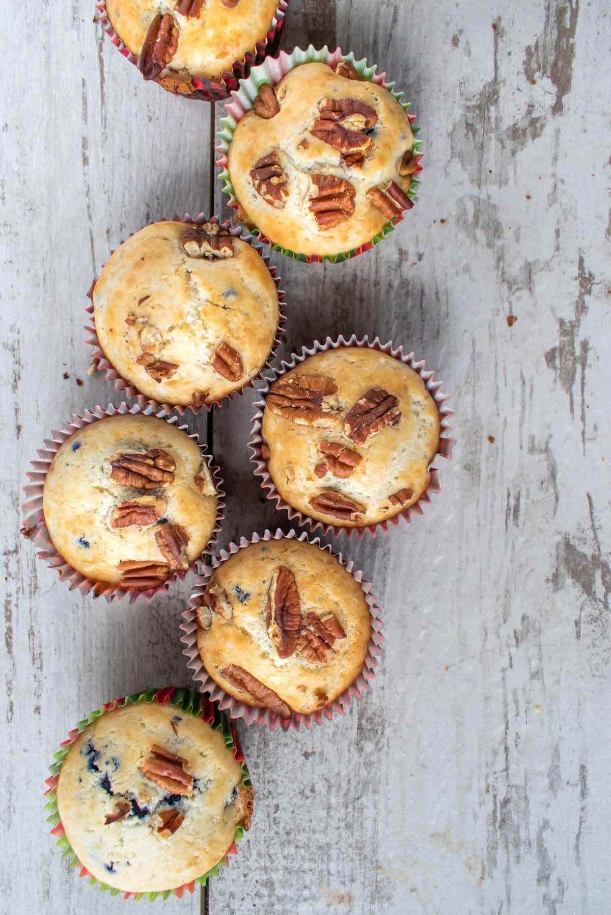 Five baked blueberry pecan muffins on a wooden surface.