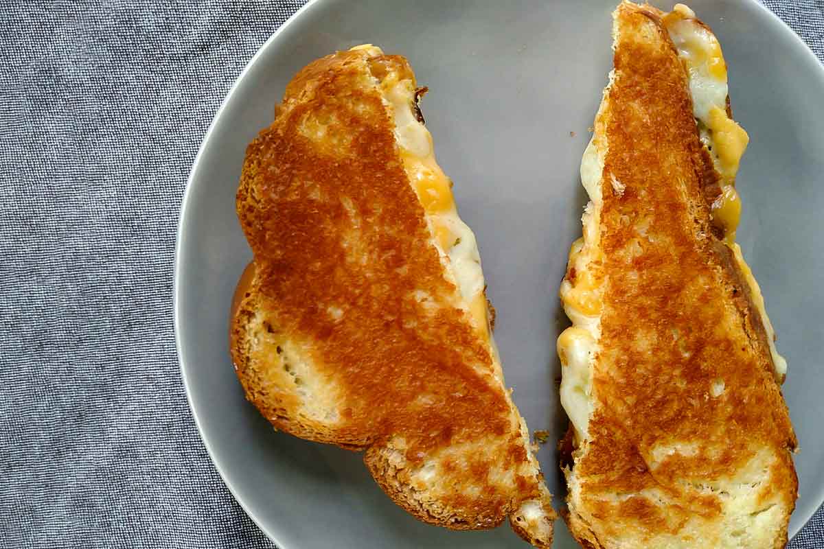 A challah grilled cheese sandwich sliced in half on a grey plate.