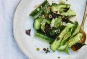A serving of Chinese smashed cucumber salad sprinkled with sesame seeds on a white plate with a gold spoon.
