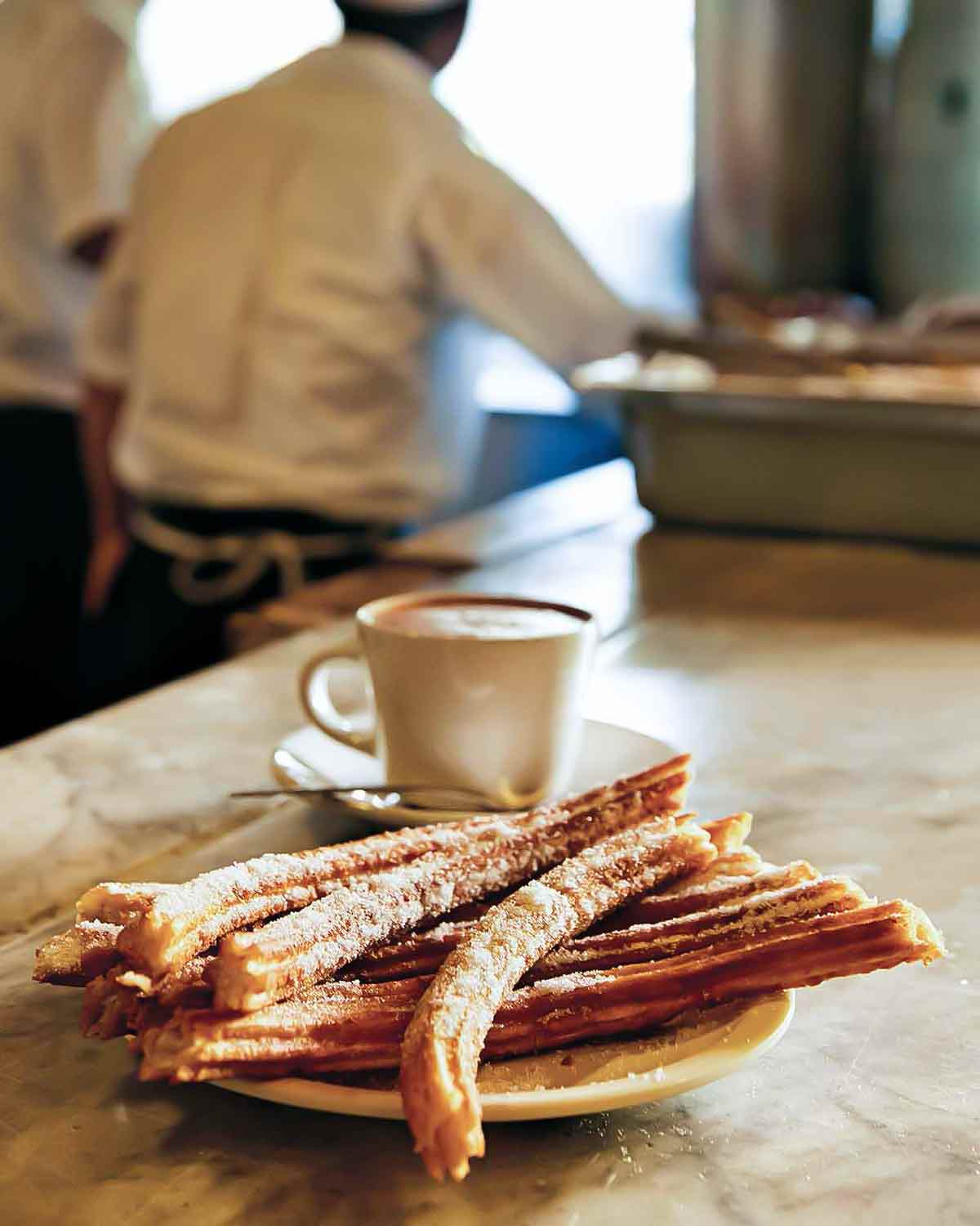 A plate of churros with a cup of hot chocolate in the background