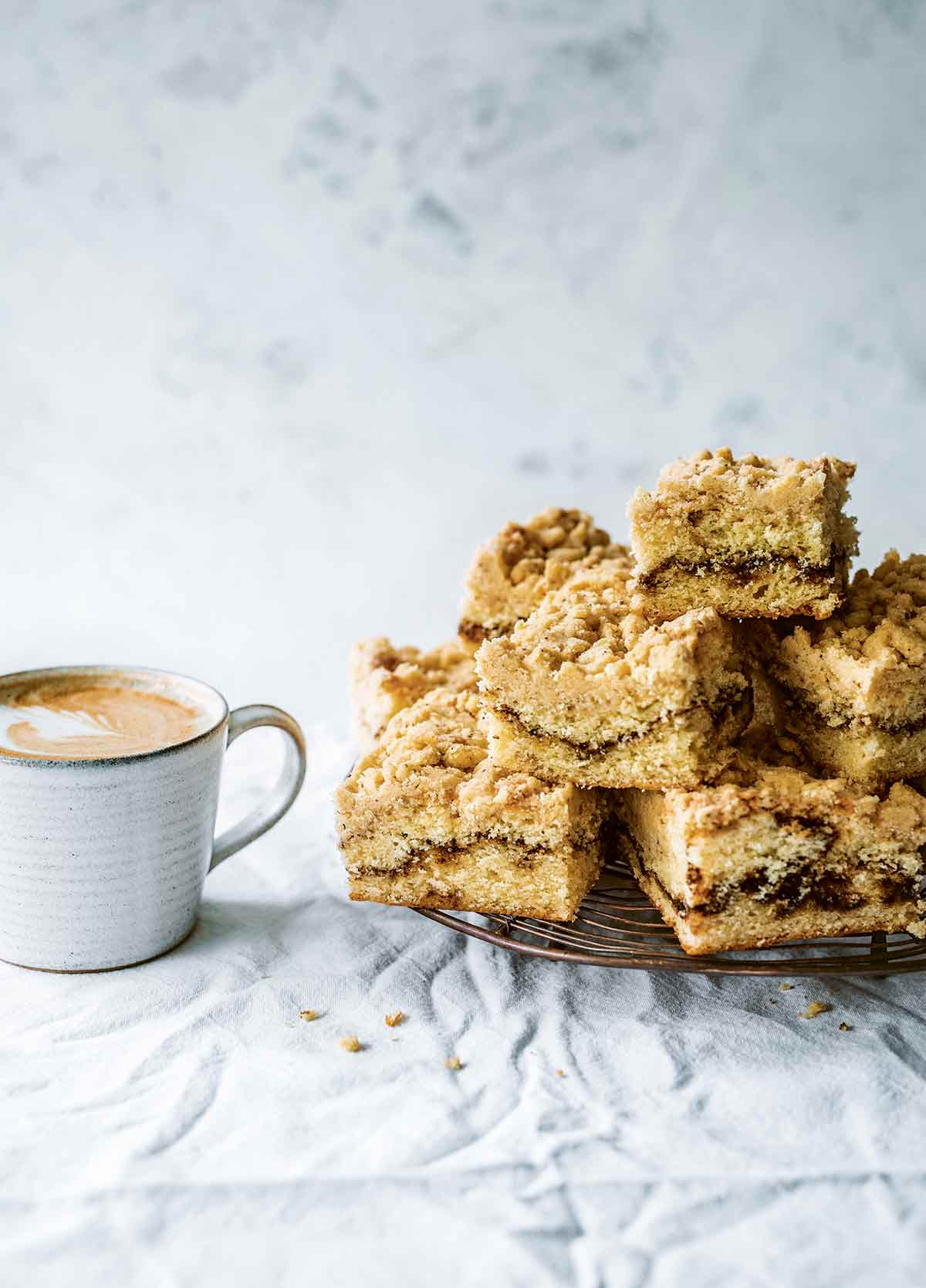 Several pieces of coffee coffee cake stacked on a wire rack, with a cup of coffee next to them.