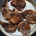 Six coffee-crusted grilled pork chops on a speckled platter.
