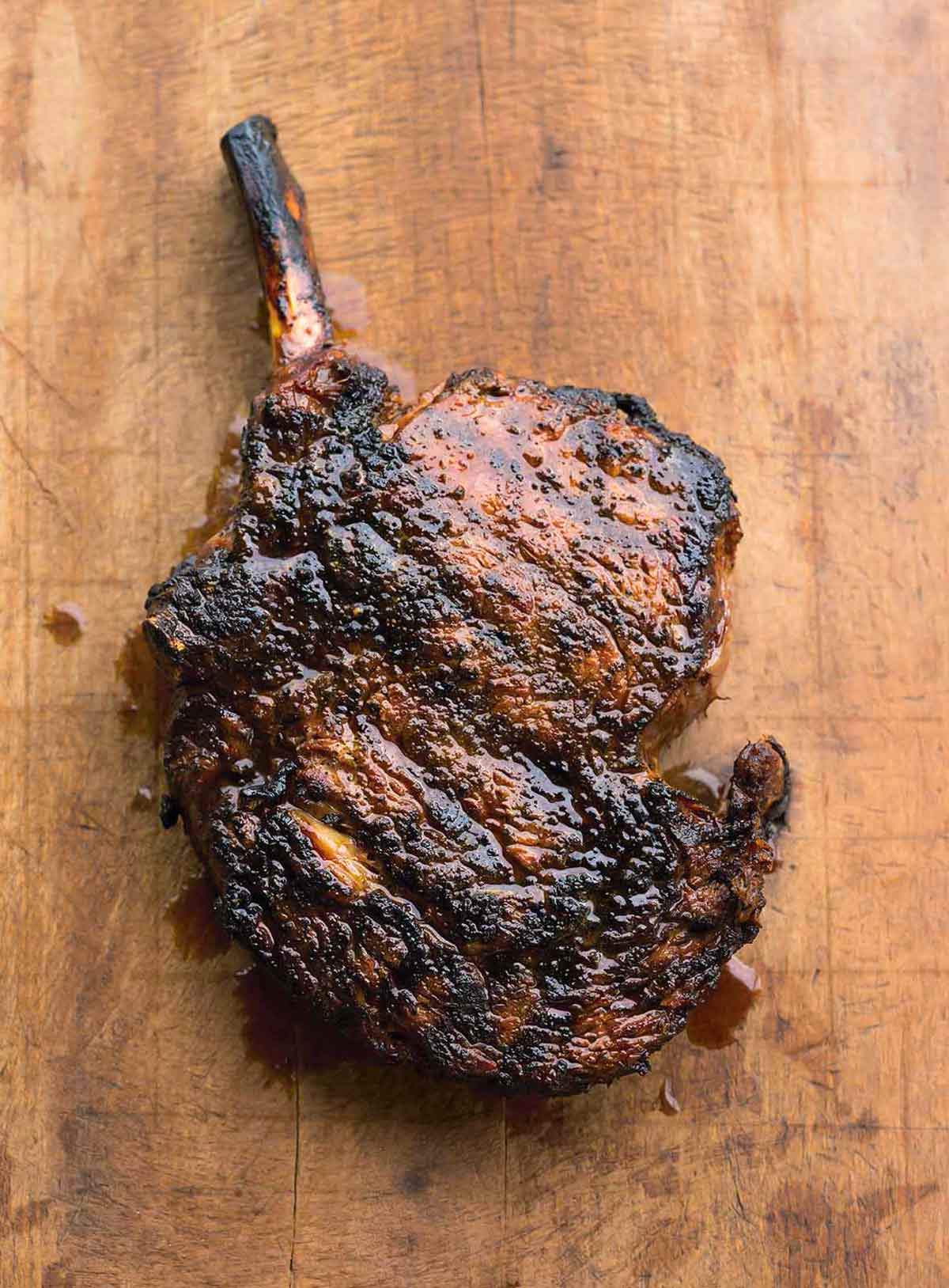 A grilled cowboy steak with coffee rub on a wooden cutting board.
