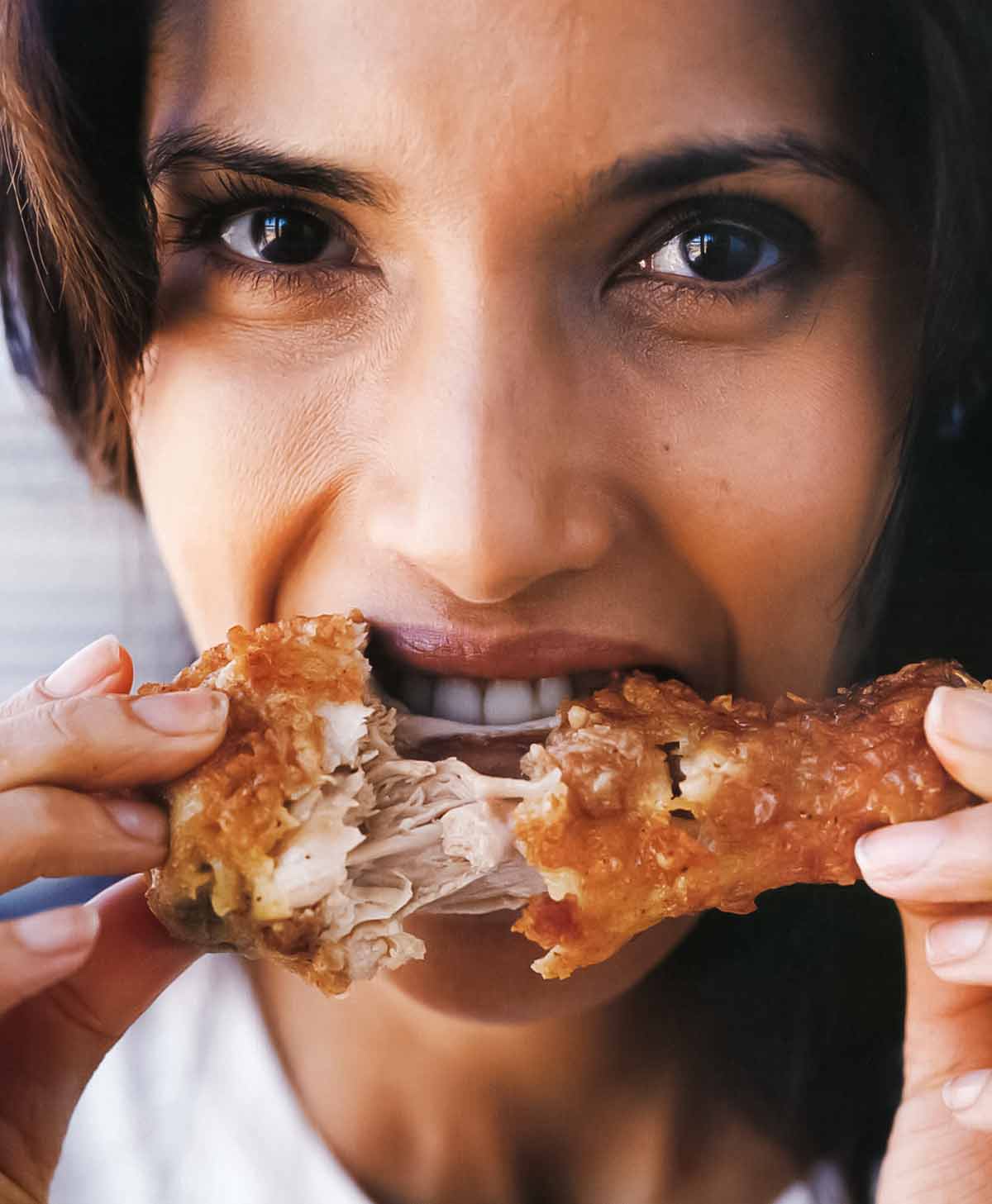 Padma eating a piece of crispy fried chicken.