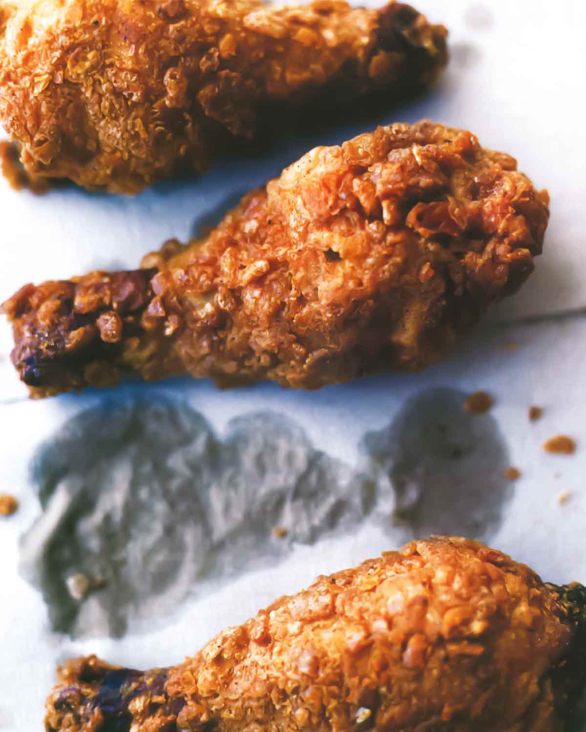 Three pieces of crispy fried chicken on grease-stained paper.