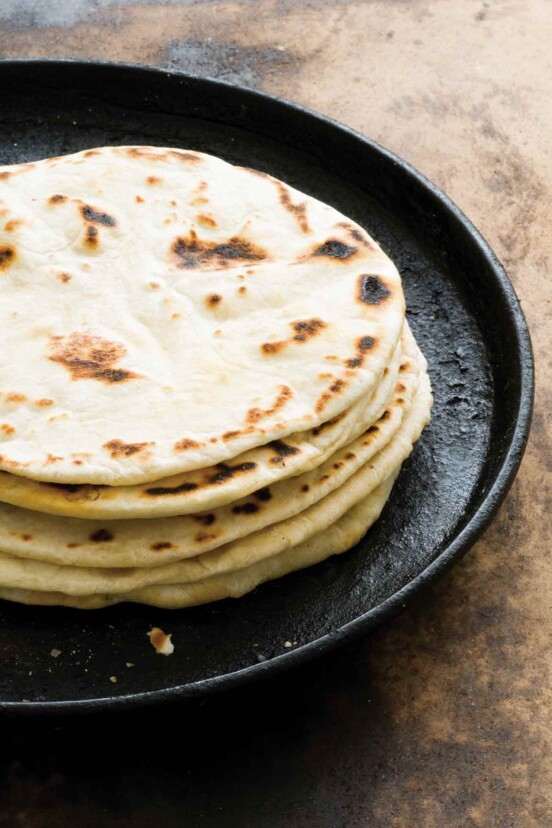 A stack of flour tortillas with bacon fat on a cast-iron skillet.