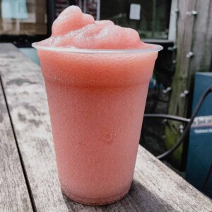 A tall plastic cup filled with frosé or frozen rosé on a wooden table.