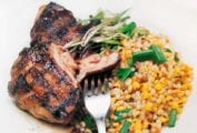A piece of grilled guinea hen with sweet corn fregula beside it, all topped with chopped scallions.