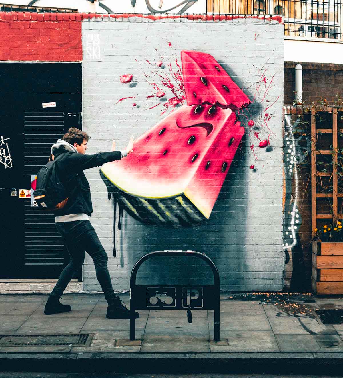 A person holding their arms up against a wall that has watermelon grafitti painted on it.