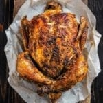 A spice-rubbed whole Instant Pot rotisserie-style chicken on a sheet of parchment paper on a wooden board.
