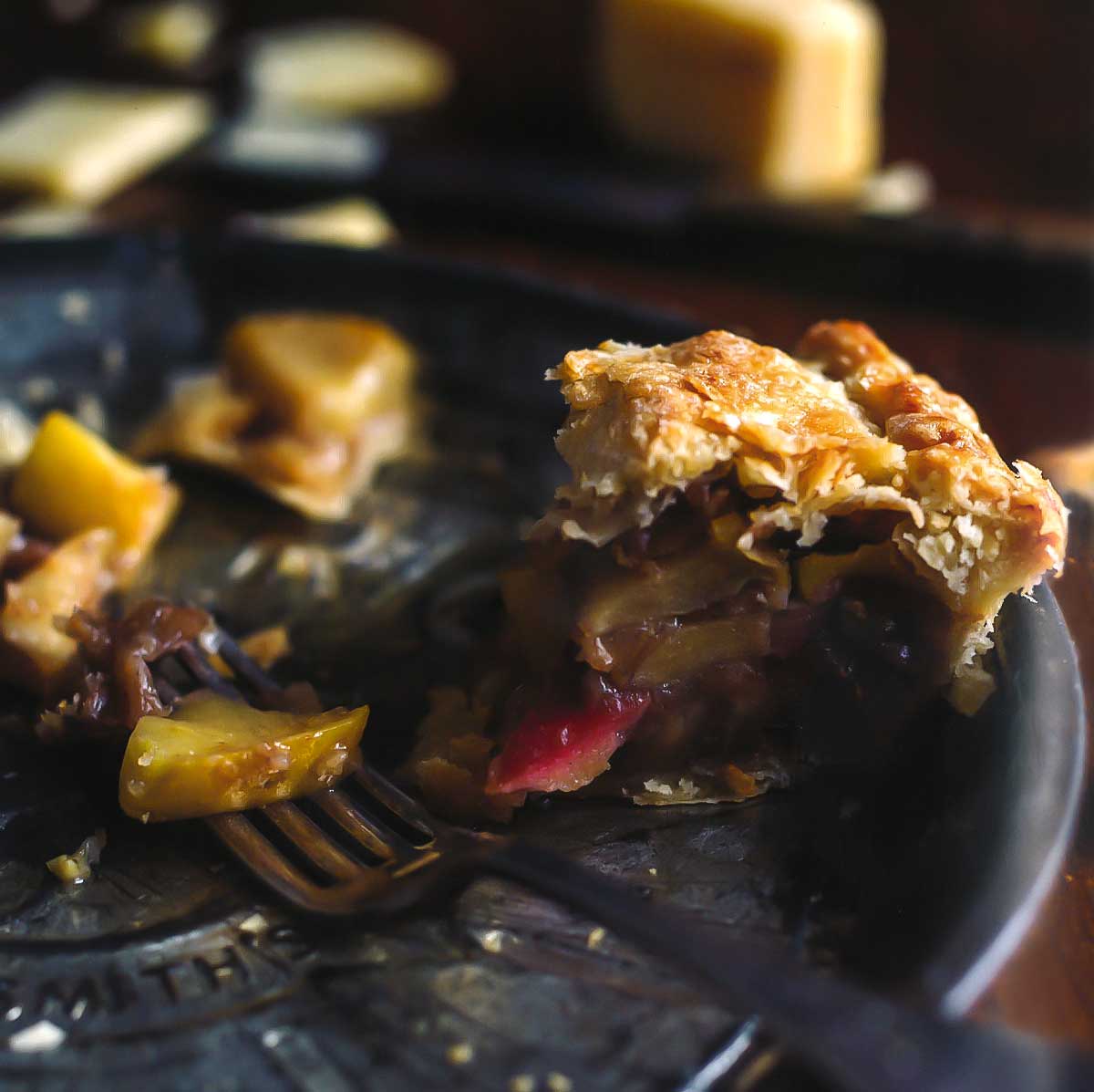 A small piece of apple pie in an almost empty pie plate with a fork and a few pieces of apple scattered around.