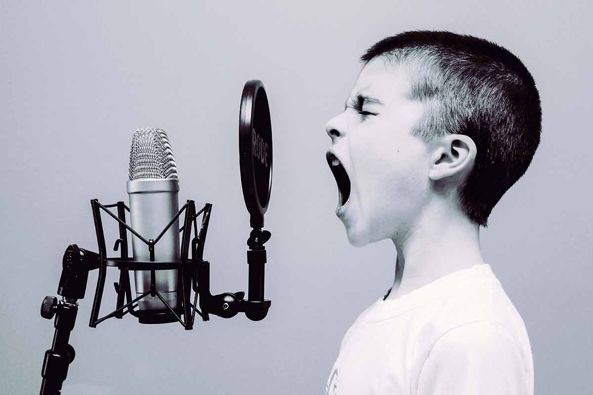 A black and white photo of a young boy yelling into a microphone.
