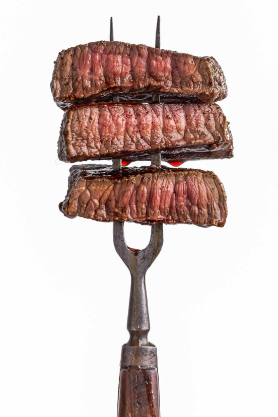 A two-pronged fork with 3 slices of perfectly cooked steak on it.