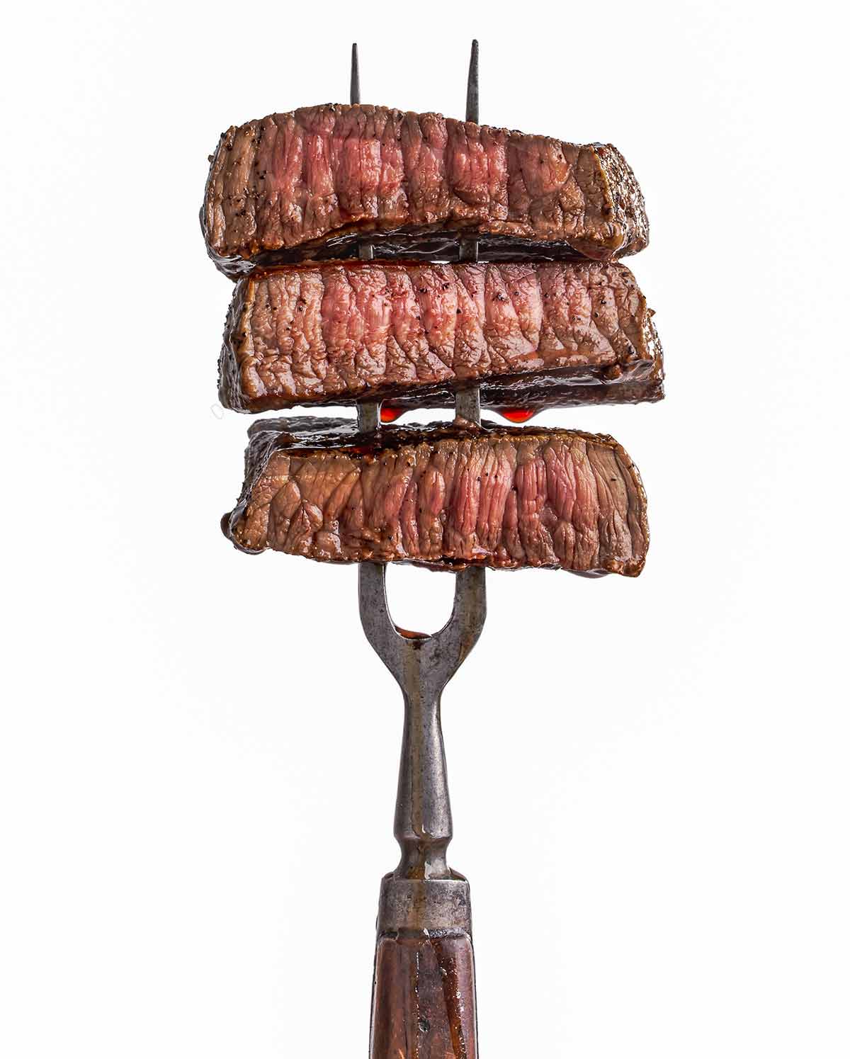 A two-pronged fork with 3 slices of perfectly cooked steak on it.