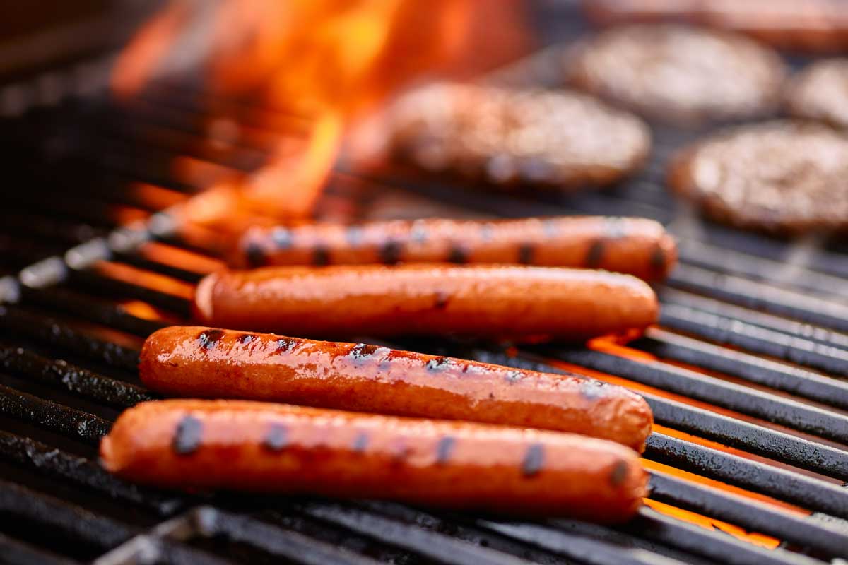 Hot dogs cooking on a grill to help explain Meathead's science of grilling.