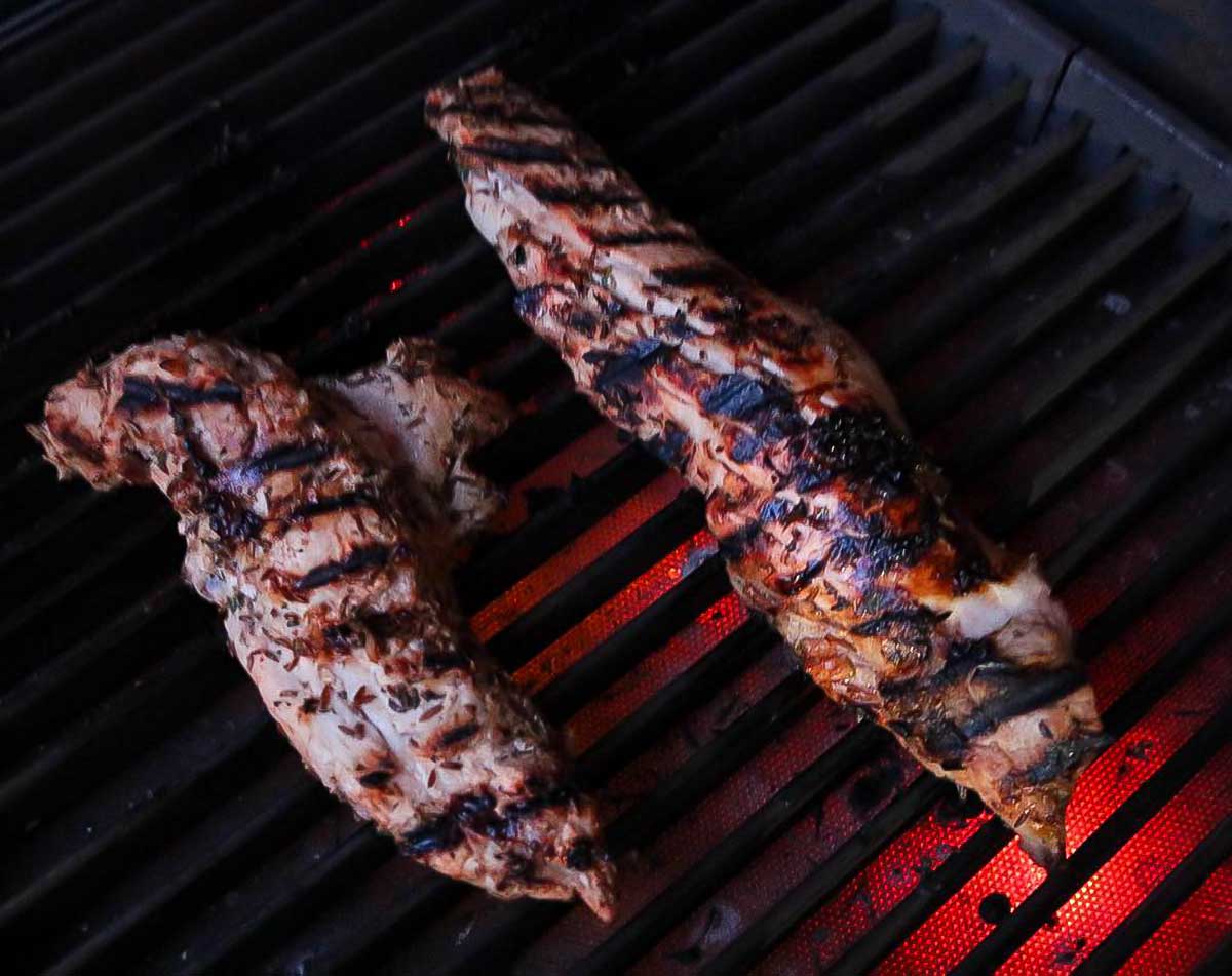 Two whole pork tenderloins with grill marks on a glowing grill.