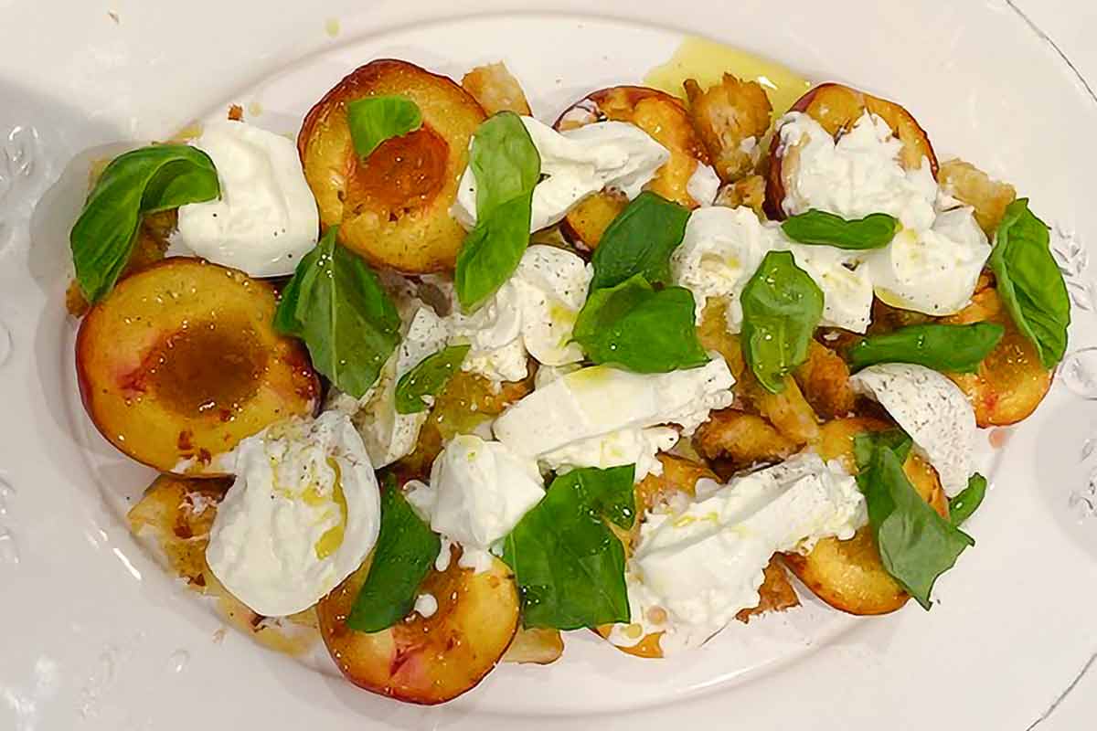 A white oval platter topped with fresh mozzarella with roasted stone fruit and toasted bread pieces.