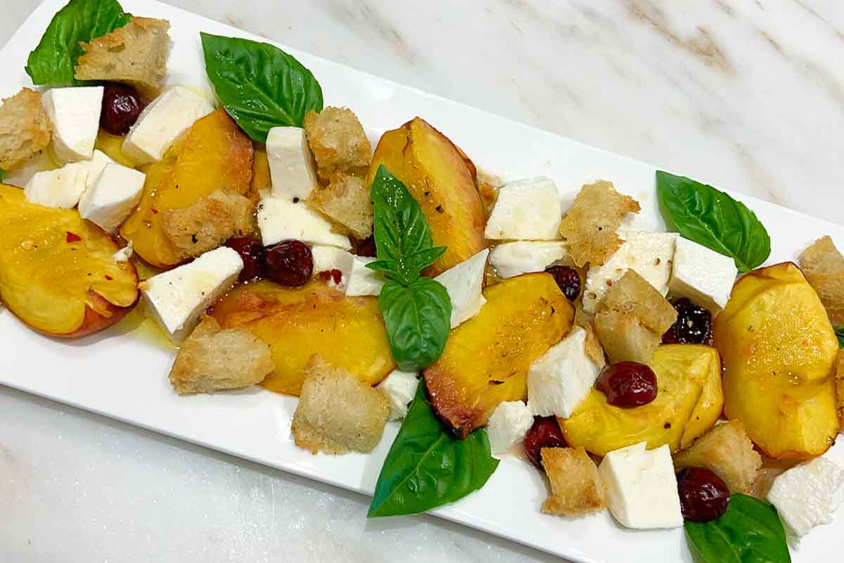 A white rectangular platter topped with mozzarella with roasted stone fruit and torn bread.