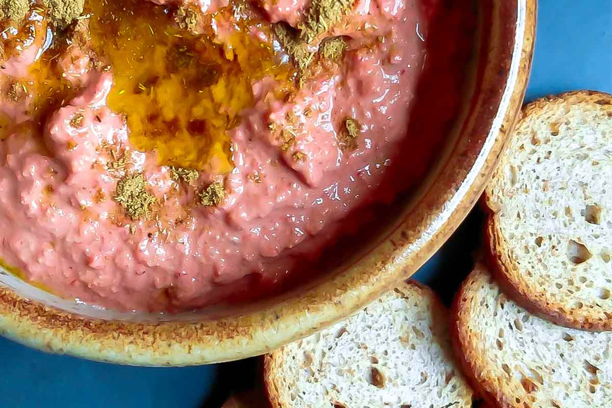 A ceramic bowl filled with muhammara and toast rounds on the side.
