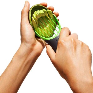 A person slicing an avocado using an OXO Good Grips avocado slicer.