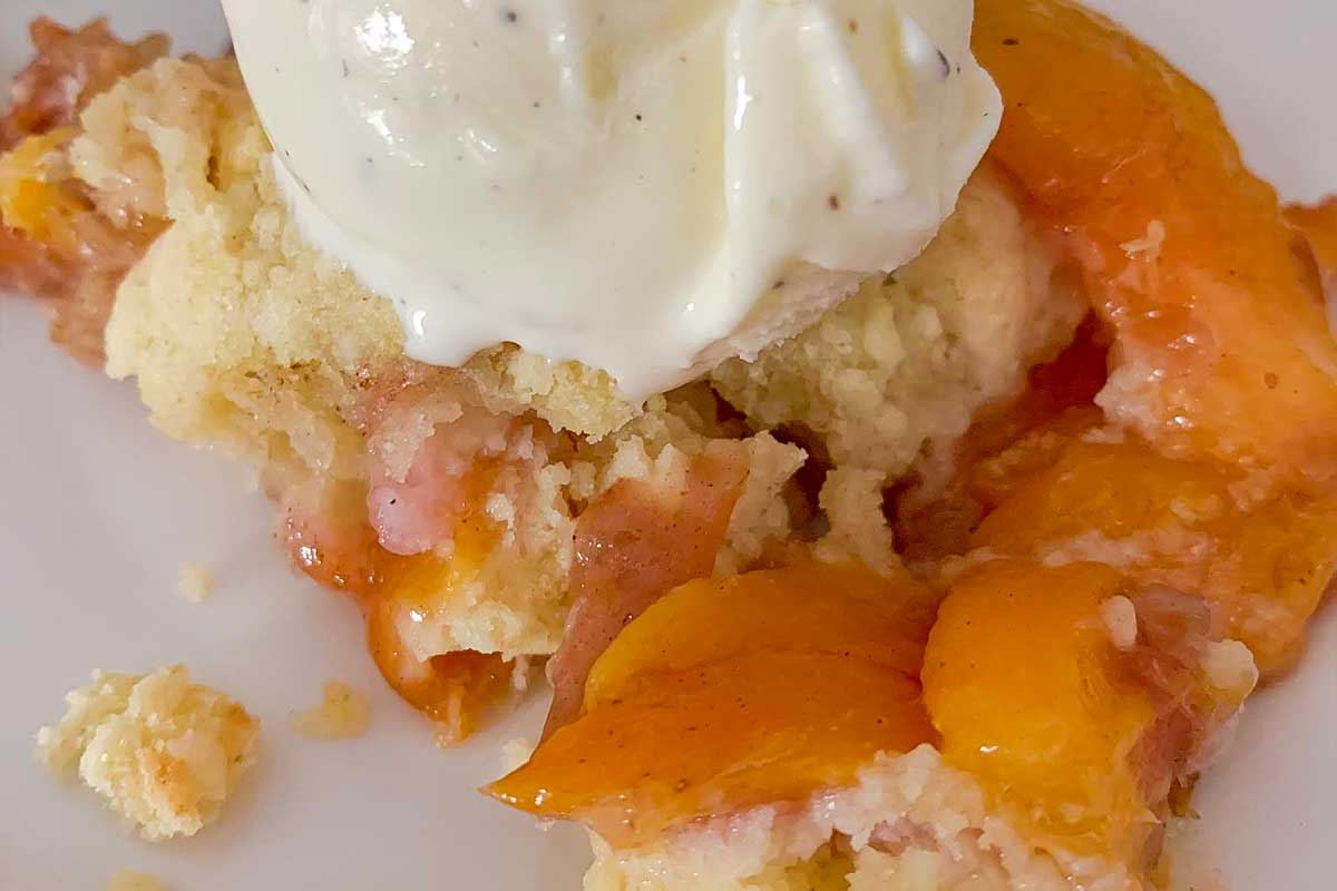 A serving of peach nectarine cobbler topped with a scoop of vanilla ice cream.