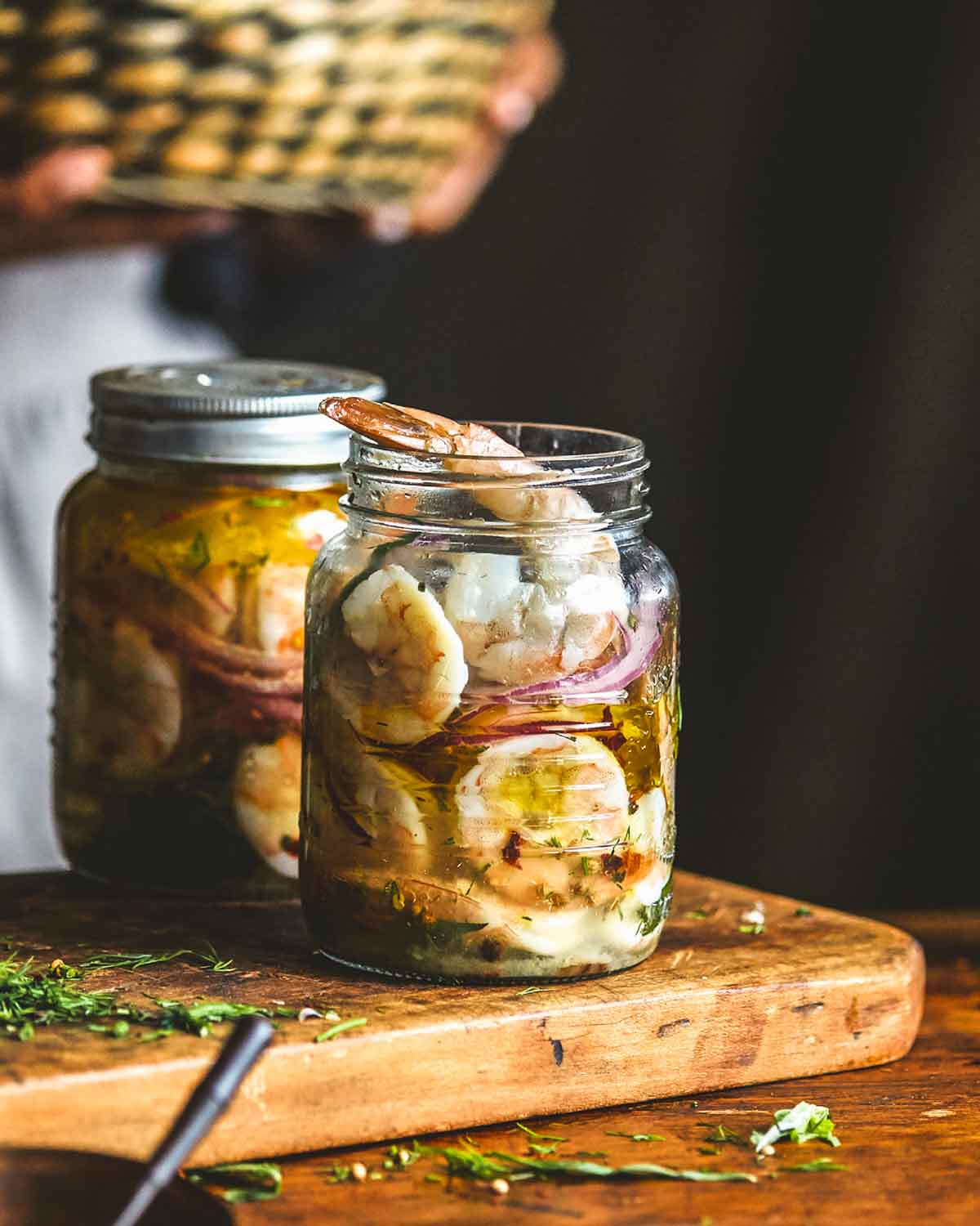 Two jars of pickled shrimp on a wooden cutting board.