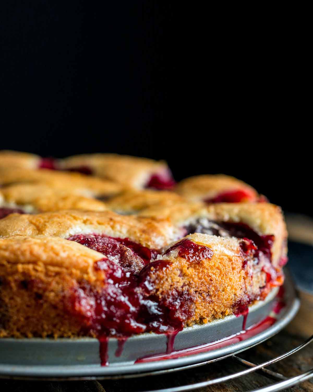 A purple plum torte with dripping juice on a baking pan, all on a cooling wrap.