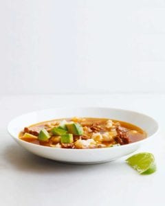 A white bowl filled with quick posole with pork topped with avocado with a lime wedge on the side.