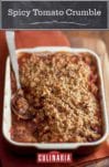 A rectangular casserole dish filled with spicy tomato crumble, and a spoon resting in it.